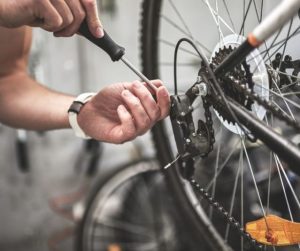 An image of two hands, one holding a screwdriver, working on bicycle rear mech